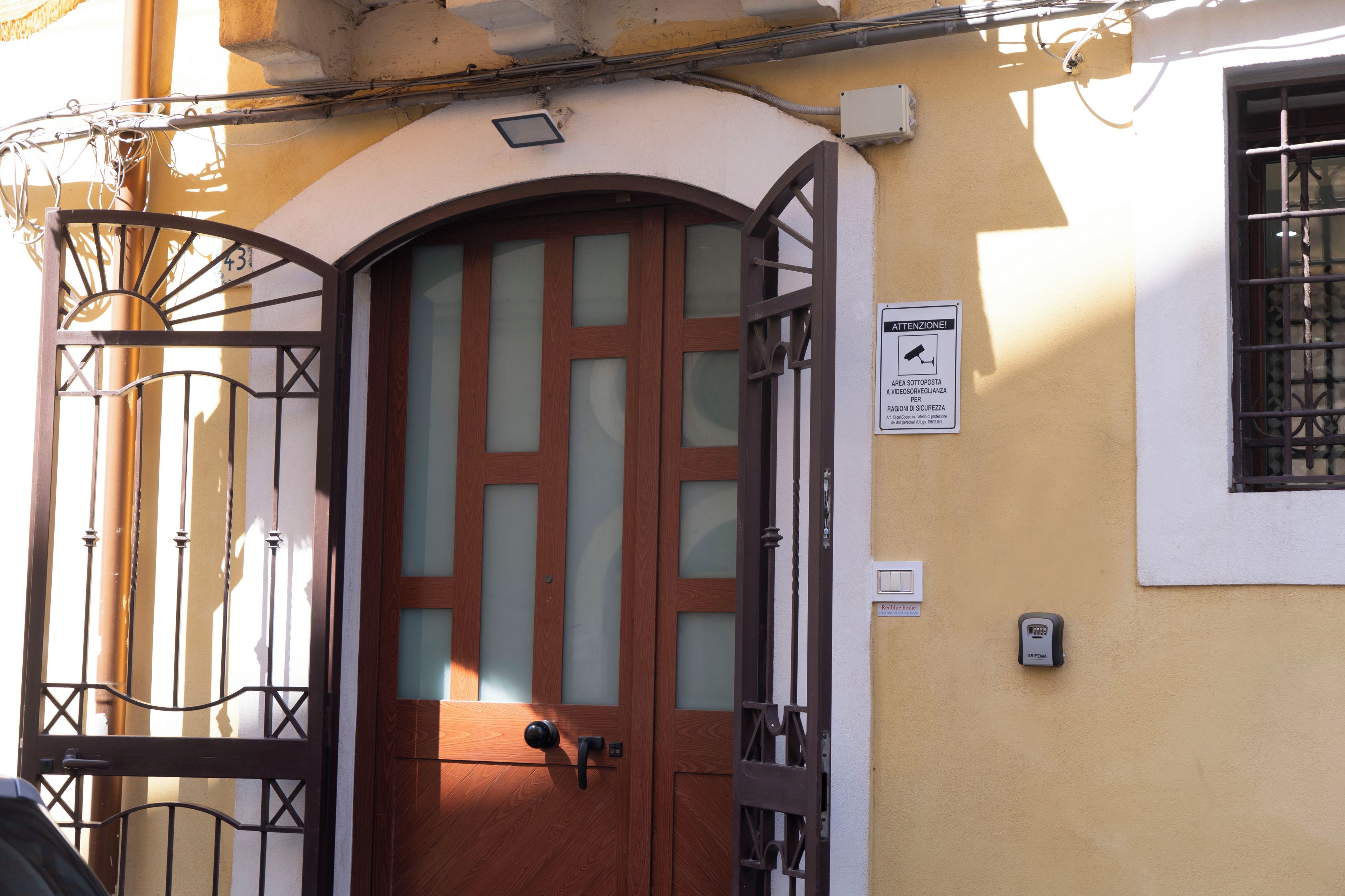 A wooden door with a glass panel, a metal gate, and a security camera on the wall.