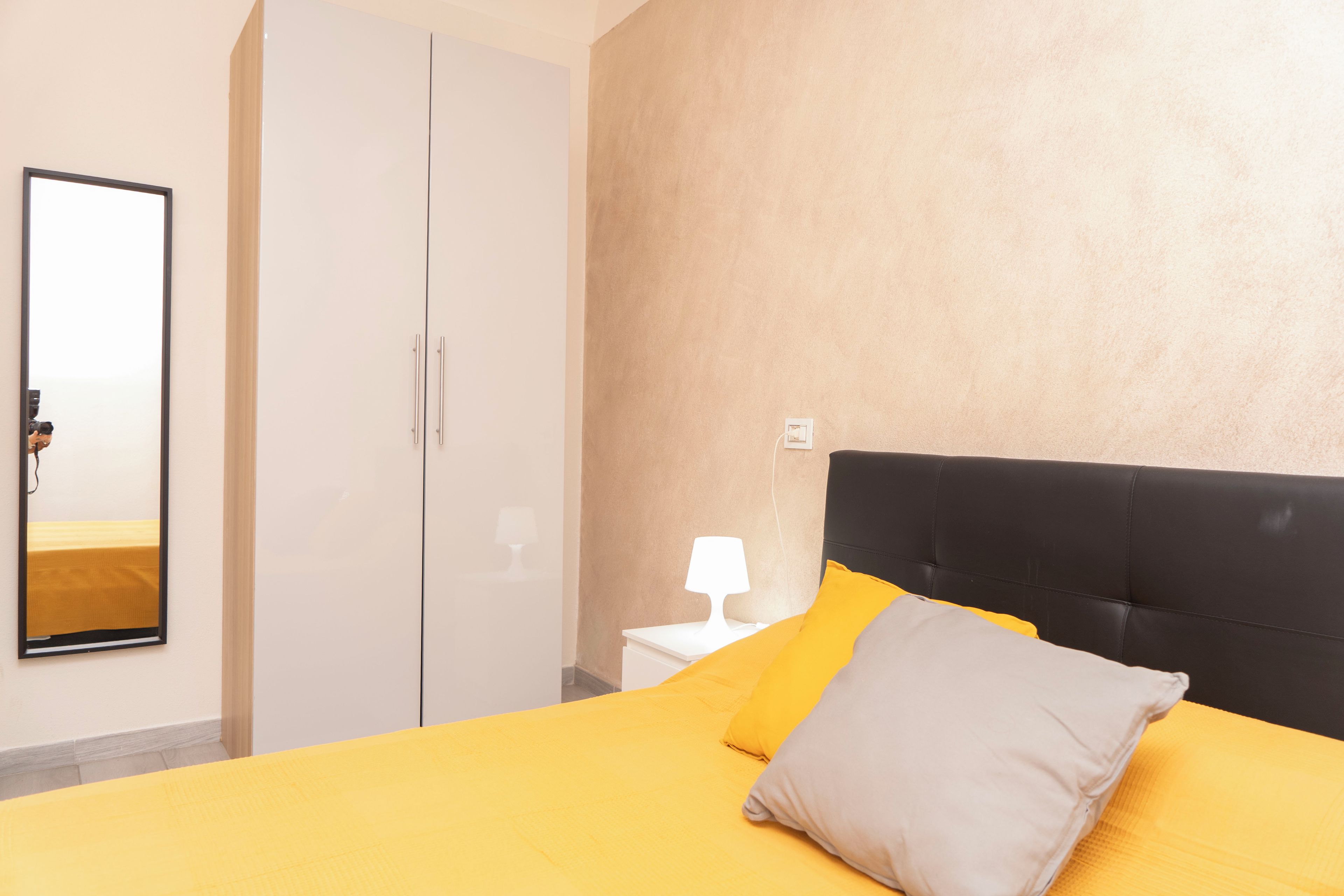 A hotel room with a bed, a wardrobe, a nightstand, and a wall-mounted lamp.