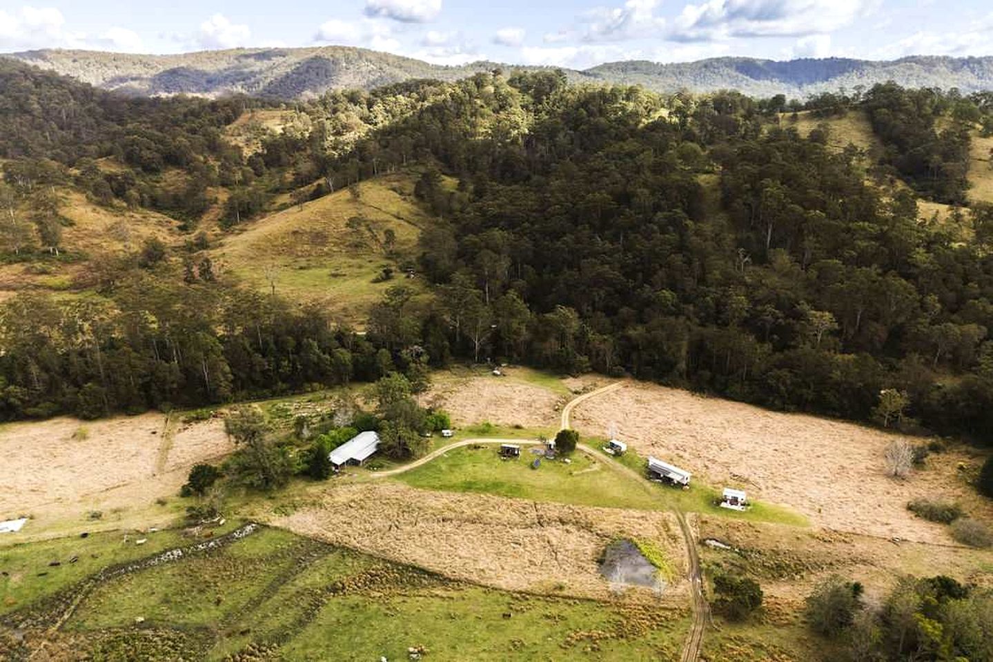 A rural landscape with a small cluster of buildings surrounded by dense forest and rolling hills.
