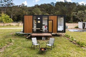 Eine kompakte, moderne Hütte mit einer Terrasse, zwei Stühlen und einer Feuerstelle.