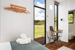 A room with a bed, a wooden drying rack, a folding chair, and a view of the outdoors.