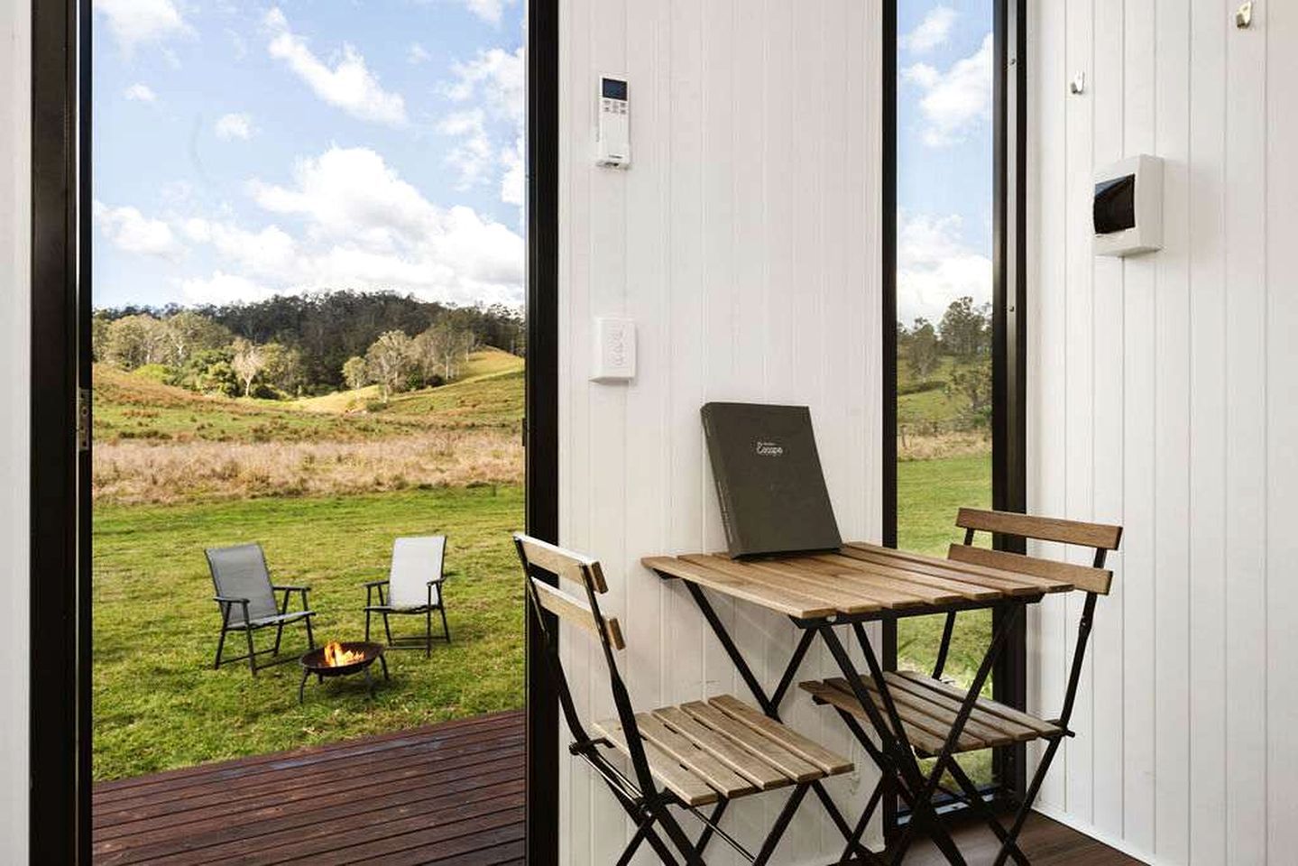Ein Zimmer mit Blick auf ein grünes Feld, ein Tisch mit Stühlen und ein Laptop auf dem Tisch.