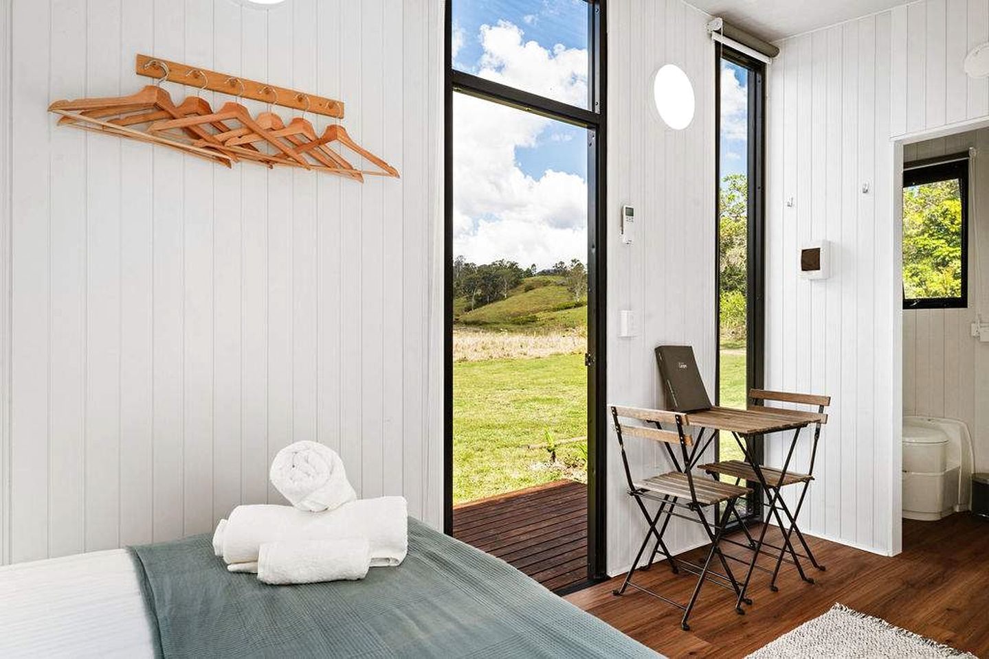 A room with a bed, a wooden drying rack, a folding chair, and a view of the outdoors.