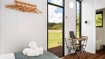 A room with a bed, a wooden drying rack, a folding chair, and a view of the outdoors.
