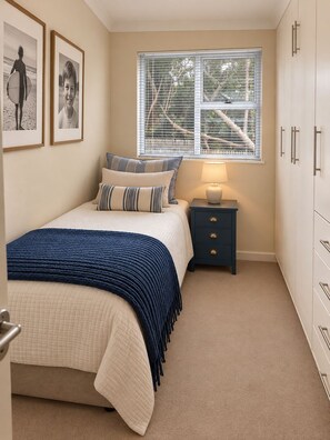 Ein Schlafzimmer mit Bett, Nachttisch, Lampe, Kleiderschrank und gerahmten Bildern an der Wand.