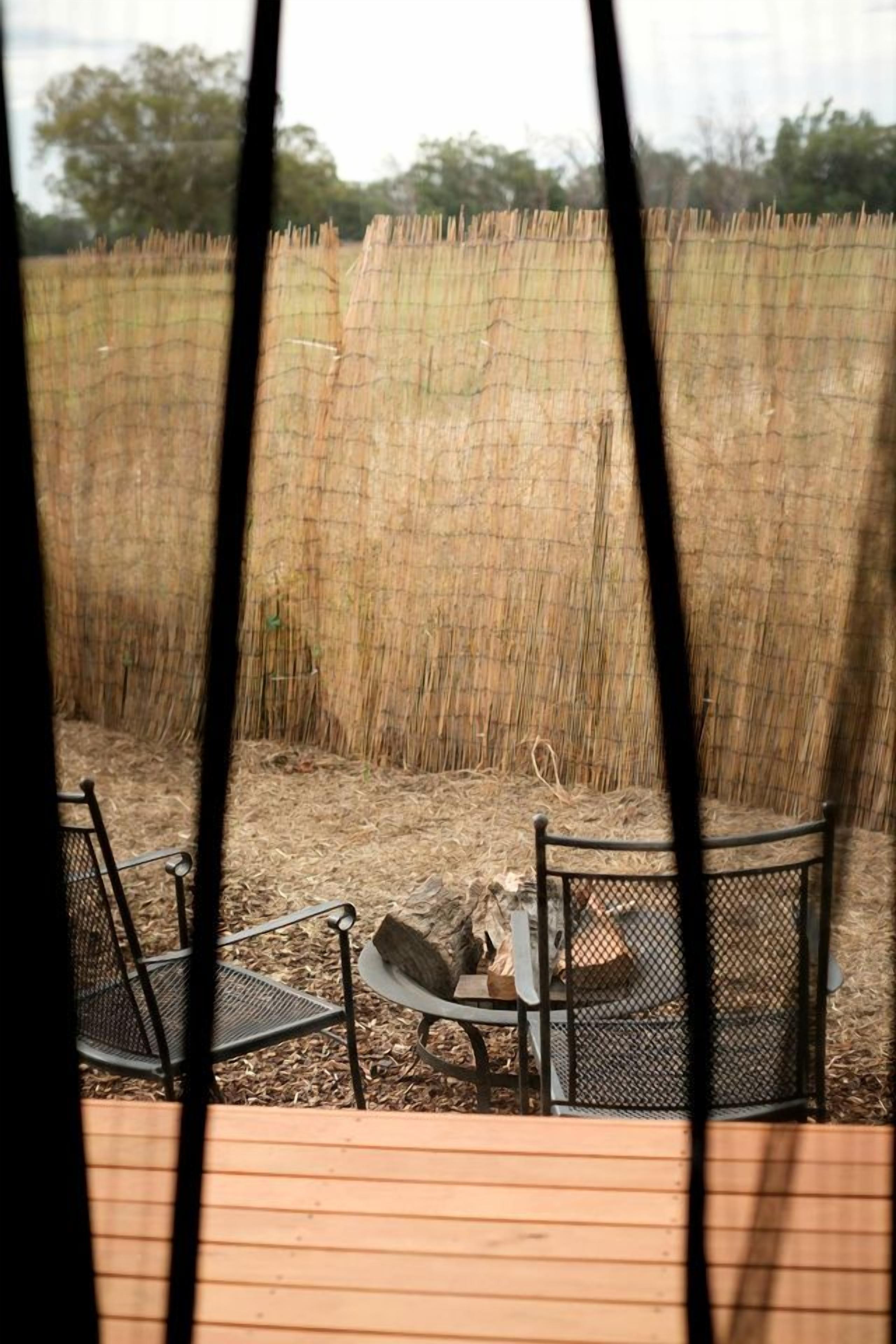 A view through a fence with a wooden deck, two metal chairs, and a table.