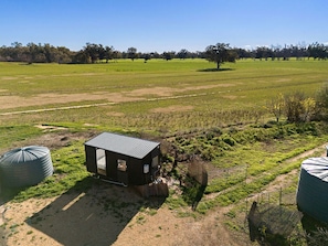A small, dark-colored building with a sloped roof, situated in a grassy field with a dirt path leading to it. There are two large cylindrical tanks on either side of the building. - Starry Night Farmstay in Forbes, New South Wales (Forbes)