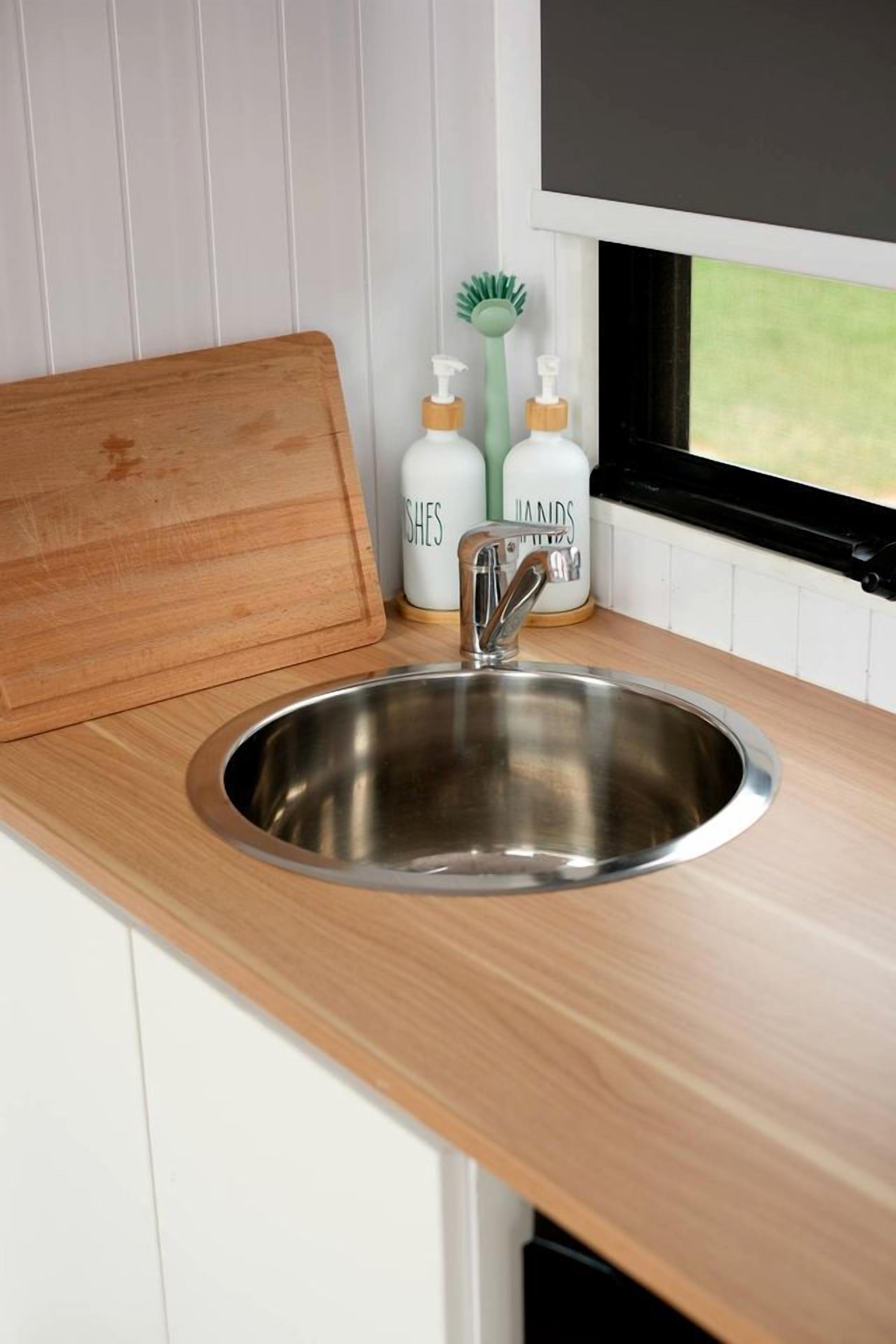 A kitchen with a stainless steel sink, wooden countertop, and a window with a view.