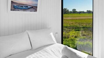 A bedroom with a bed, a window with a view of a field, and an air conditioning unit.