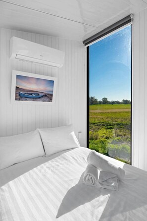 A bedroom with a bed, a window with a view of a field, and an air conditioning unit. - Starry Night Farmstay in Forbes, New South Wales (Forbes)
