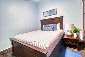 A bedroom with a wooden bed, a nightstand with a lamp, and a small potted plant. - Spacious unit in the historical Zonal Colonial with a view of the Caribbean Sea. (CIUDAD COLONIAL)