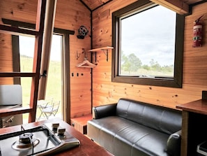 A cozy cabin interior with a leather couch, wooden walls, a window, and a table with a kettle.