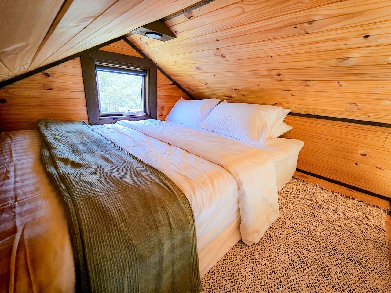 A bedroom with a bed, a window, and wooden walls.