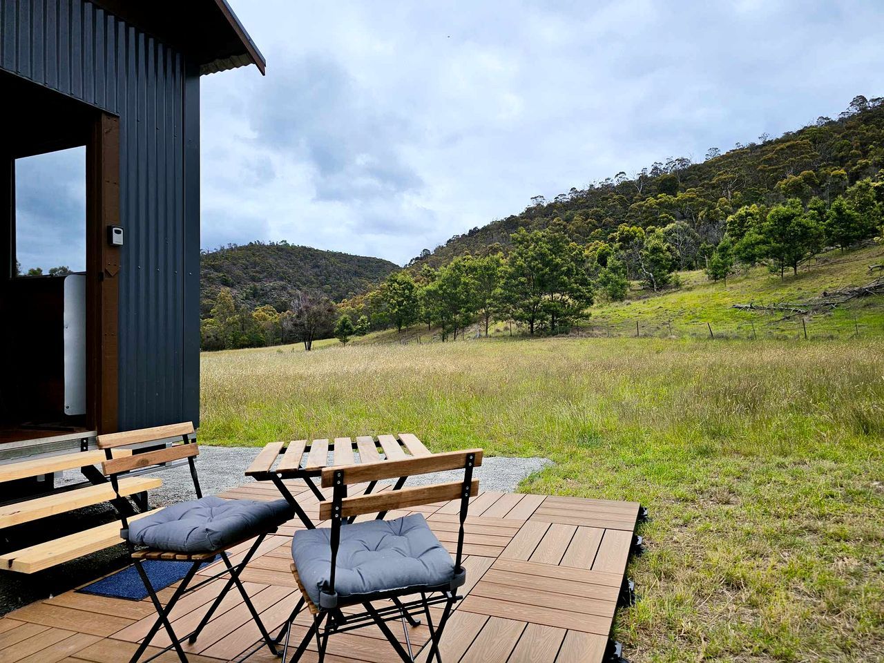 Une terrasse extérieure en bois, avec une table et des chaises, donnant sur un champ verdoyant et des collines.