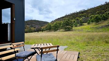 Une terrasse extérieure en bois, avec une table et des chaises, donnant sur un champ verdoyant et des collines.