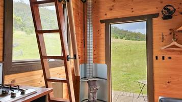 A wooden interior with a stove, a ladder, and a view of the outdoors.