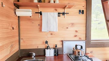 Une cuisine compacte avec un intérieur en bois, un évier en acier inoxydable, une cuisinière à gaz et une fenêtre laissant entrer la lumière naturelle.