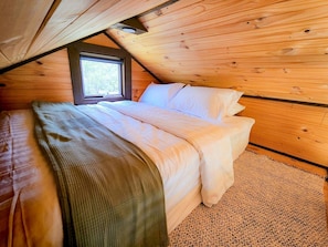 A bedroom with a bed, a window, and wooden walls.