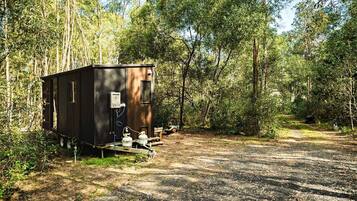 Ein kleiner, dunkel gefärbter Wohnmobil mit Warmwasserbereiter und Propanbehälter, abseits auf einem Feldweg inmitten dicht bewaldeter Landschaft geparkt.