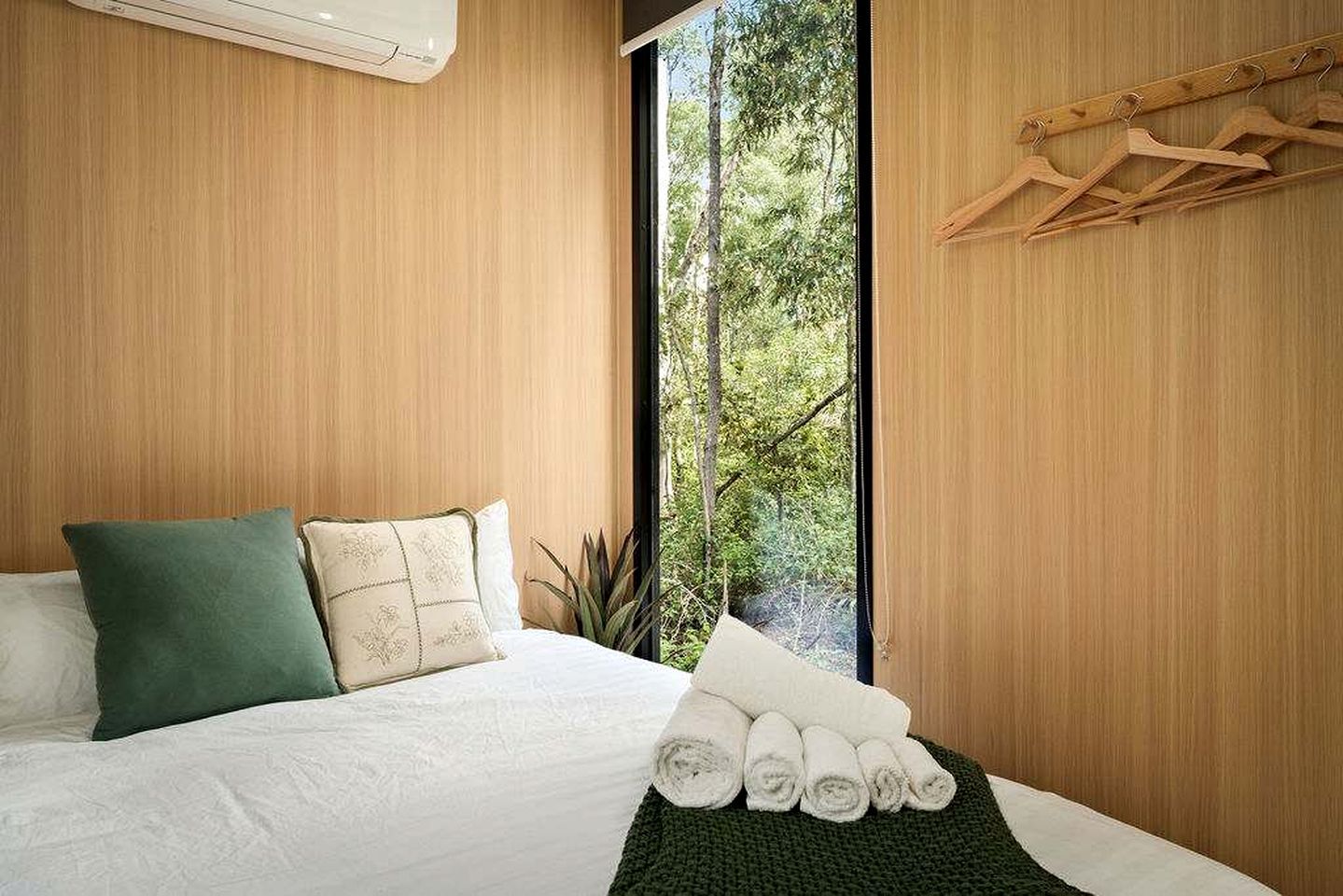 Quarto com cama, almofadas, janela e planta.