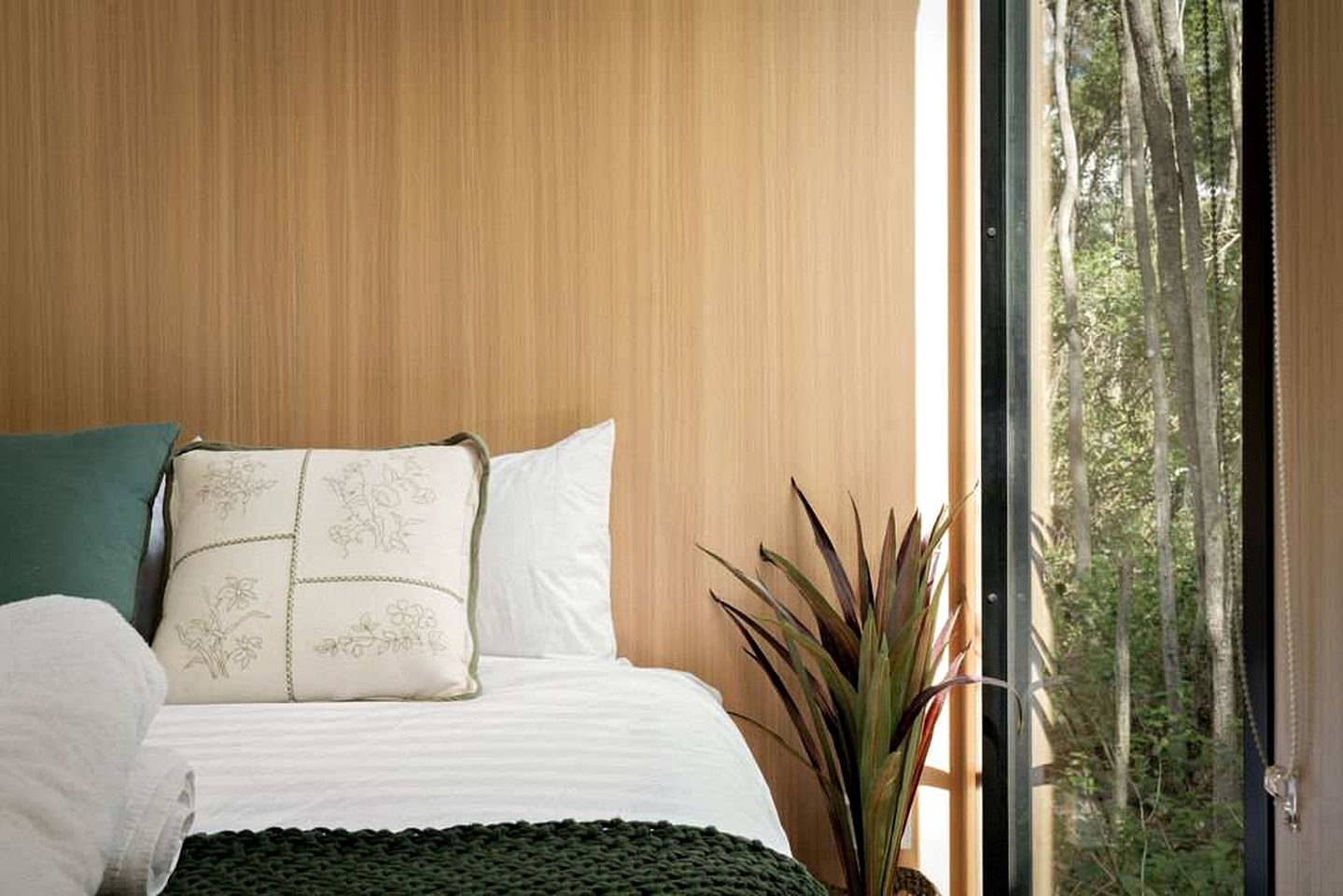 Quarto com cama, travesseiros e vista para árvores pela janela.