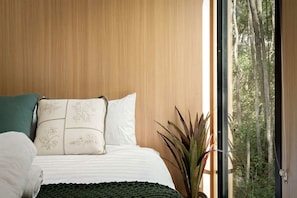 A bedroom with a bed, pillows, and a view of trees through a window.