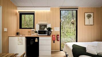 A compact room with a kitchenette, a bed, and a large window.