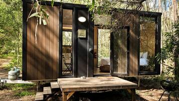 Uma cabana pequena com fachada de madeira, uma porta e um banco na frente.