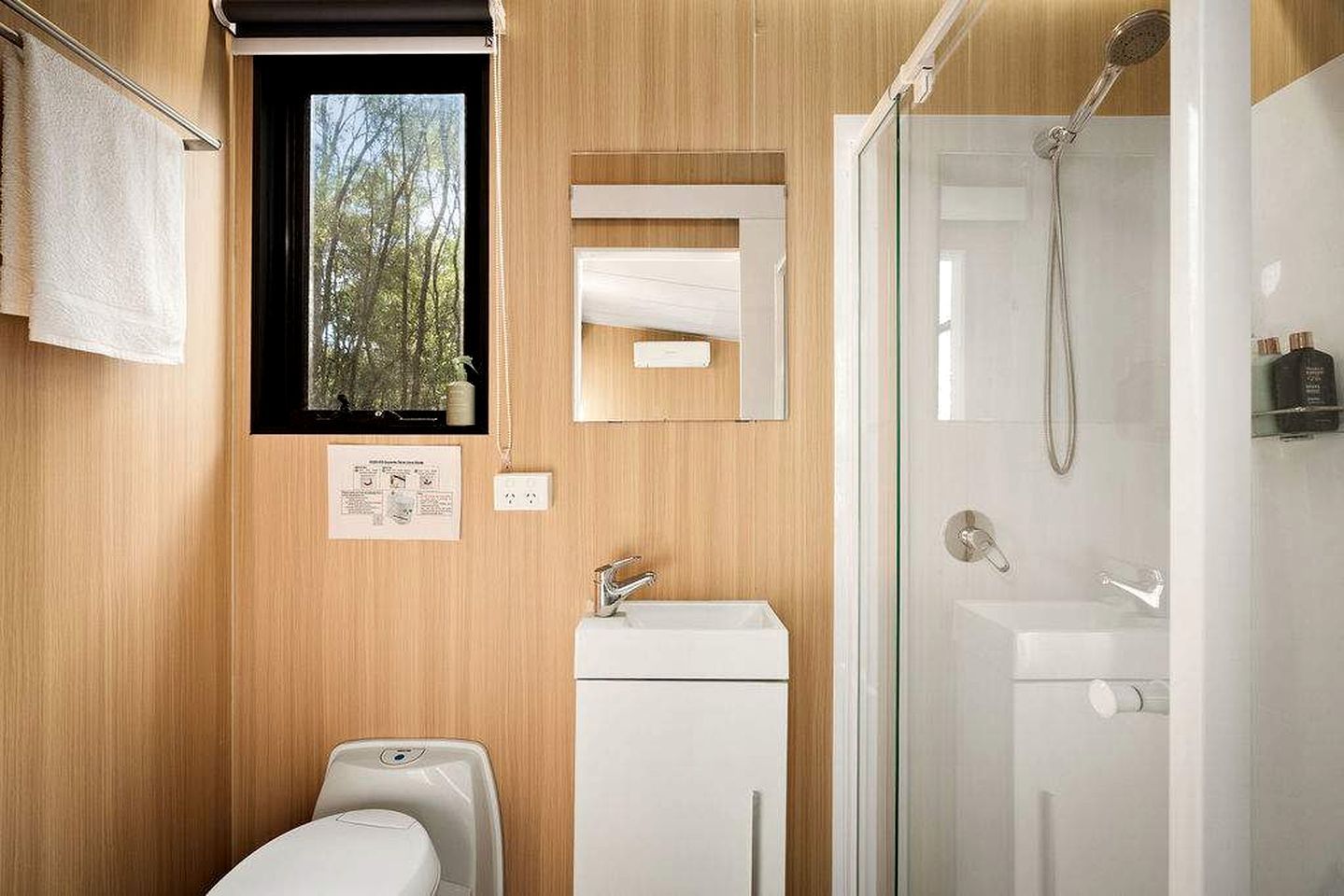 A modern bathroom with a wooden wall, a window, a mirror, a sink, and a shower.