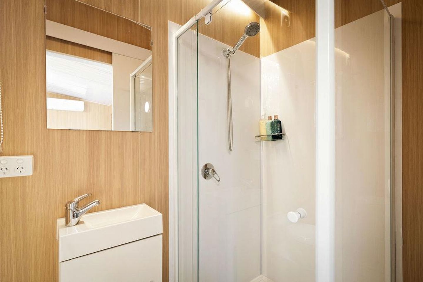 A modern bathroom with a glass-enclosed shower, a white sink, and a mirror above the sink.
