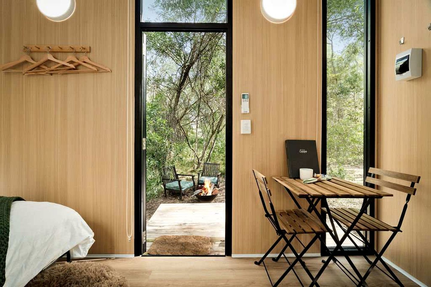 Une pièce avec un lit, une table et des chaises, un foyer extérieur et une vue sur les arbres.