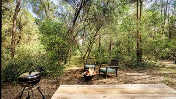 A wooden deck with a fire pit and two chairs in a forested area.