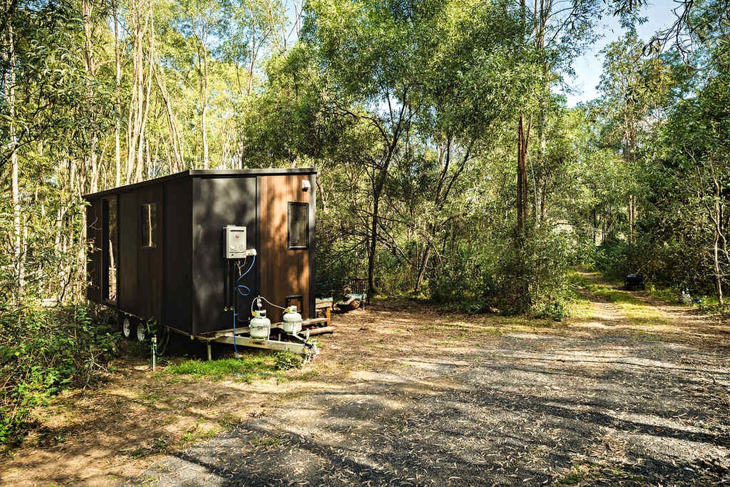 Ein kleiner, dunkel gefärbter Wohnmobil mit Warmwasserbereiter und Propanbehälter, abseits auf einem Feldweg inmitten dicht bewaldeter Landschaft geparkt.