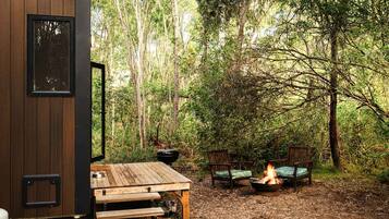 A wooden deck with a fire pit and seating area surrounded by a forest.