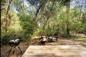 Um deck de madeira com uma lareira e duas cadeiras em uma área arborizada.