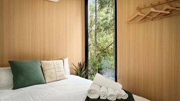 Un dormitorio con cama, almohadas, una ventana y una planta.