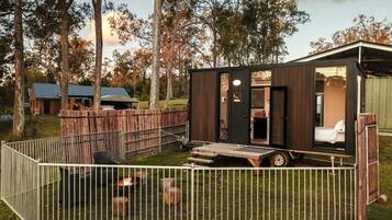 A small cabin with a deck, a fire pit, and a fenced yard.