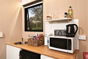 A kitchenette with a microwave, a basket of snacks, a kettle, and a window with a view of trees.
