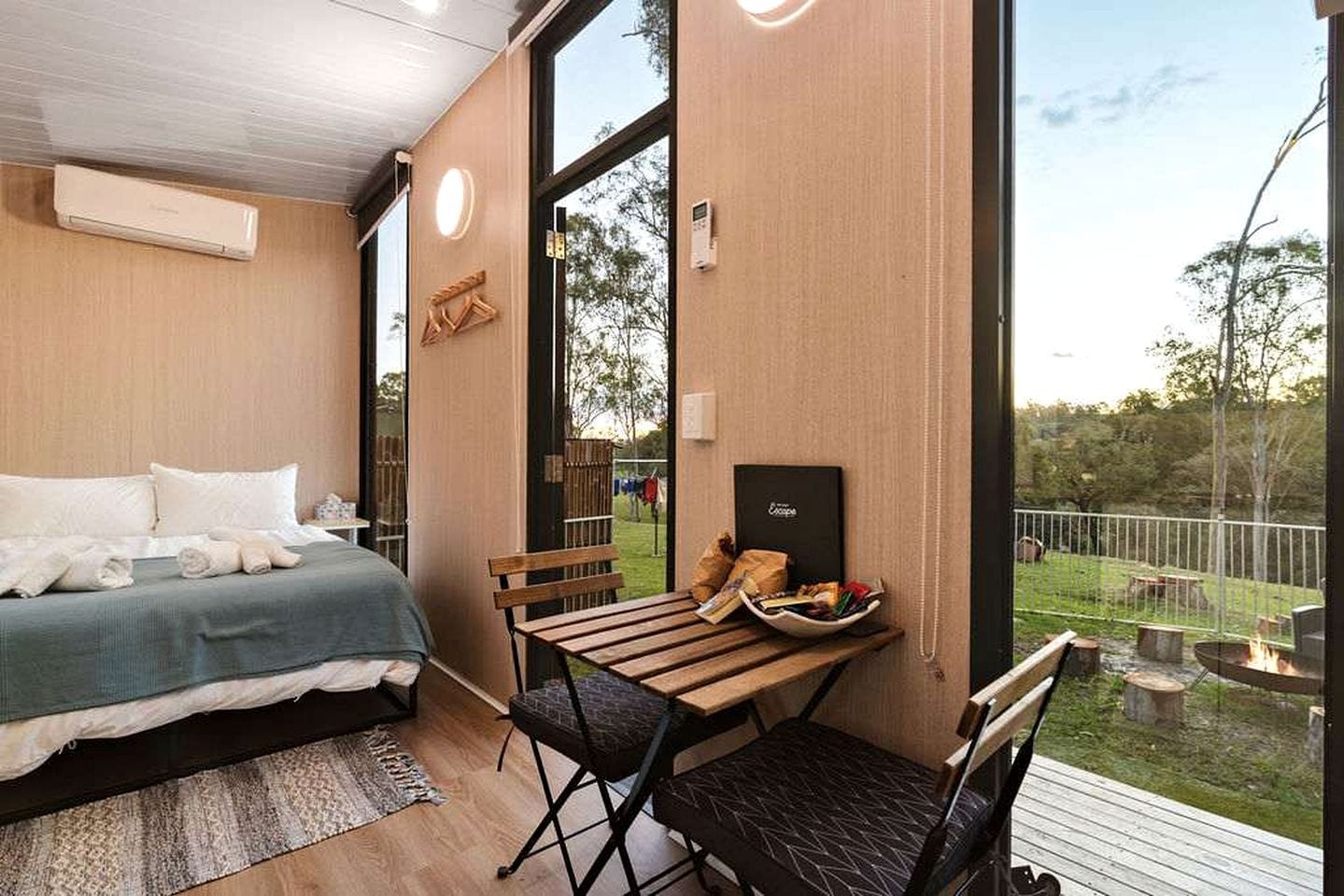 Quarto com cama, mesa e cadeiras, e vista para o exterior.