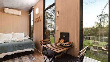 Quarto com cama, mesa e cadeiras, e vista para o exterior.