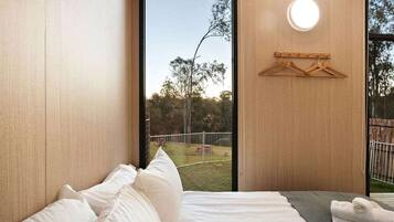 A bedroom with a large window, a bed with white linens, a towel on the side, and a wooden hanger on the wall.