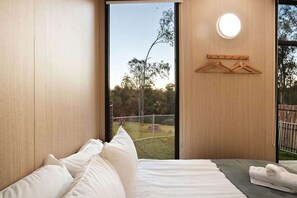 A bedroom with a large window, a bed with white linens, a towel on the side, and a wooden hanger on the wall.