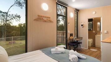A bedroom with a bed, a table with chairs, a bathroom, and a balcony with a fence.