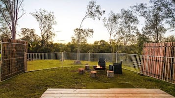 Ein umzäunter Garten mit Feuerstelle, Sitzgelegenheiten und einer Holzterrasse.