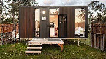 Uma cabana compacta com entrada por porta deslizante, uma pequena área de estar externa e cozinha à vista.