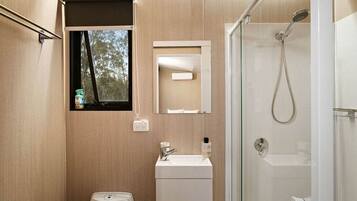A bathroom with a window, a mirror, a sink, a toilet, and a shower.