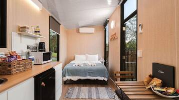 Quarto de hotel compacto com cama, mesa de cabeceira e pequeno espaço de cozinha.