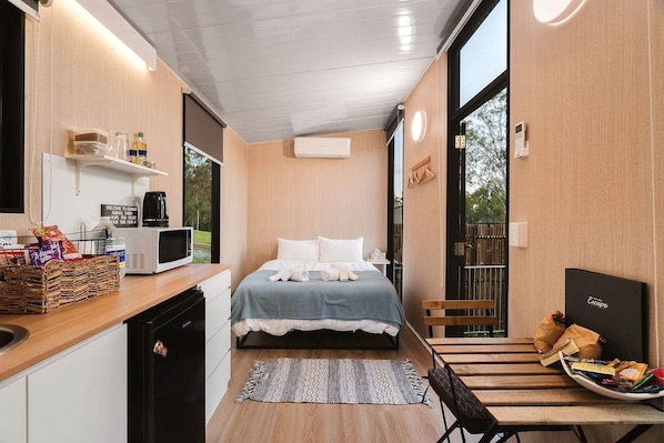 Habitación de hotel compacta con cama, mesita de noche y una pequeña kitchenette.