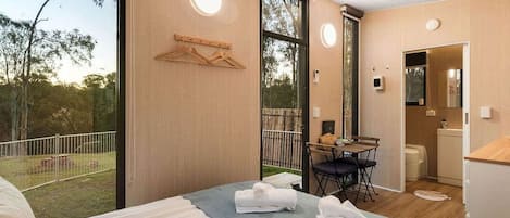 A bedroom with a bed, a table with chairs, a bathroom, and a balcony with a fence.