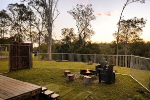 A fenced backyard with a fire pit, outdoor seating, and a wooden deck.